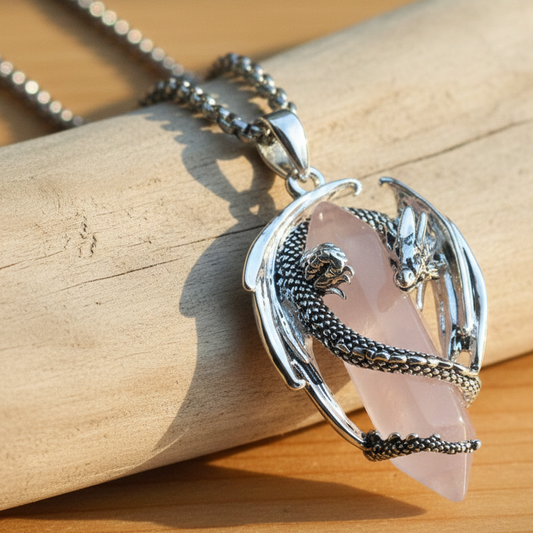 Collana con ciondolo a forma di drago che avvolge u prisma di quazo rosa. La collana misura 45 cm ed è in acciaio, mentre il ciondolo è in rame placcato argento rodiato per garantirne durata e resistenza nel tempo.