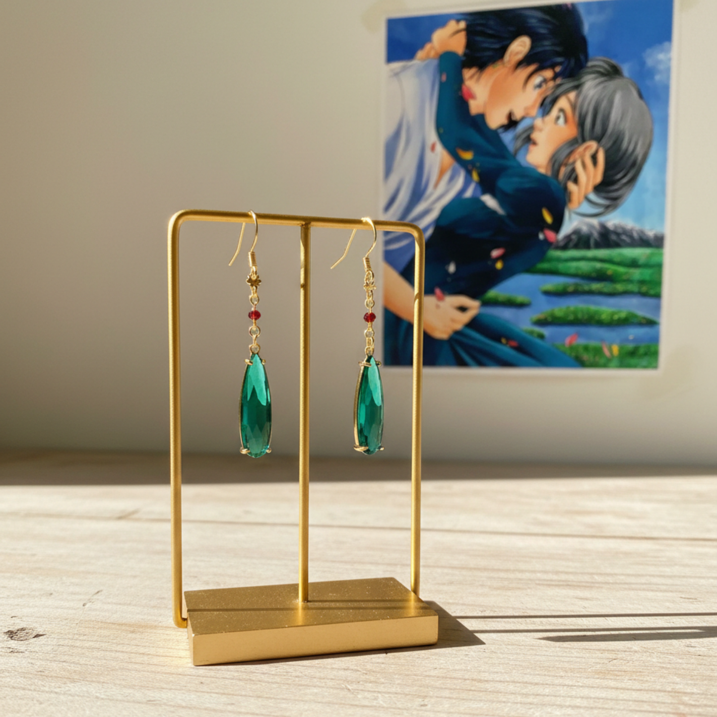 Coppia di orecchini a monachella dorati con goccia pendente verde smeraldo e piccolo cristallo rosso, ispirati al personaggio Howl de Il Castello Errante di Howl, gioielli cosplay eleganti.