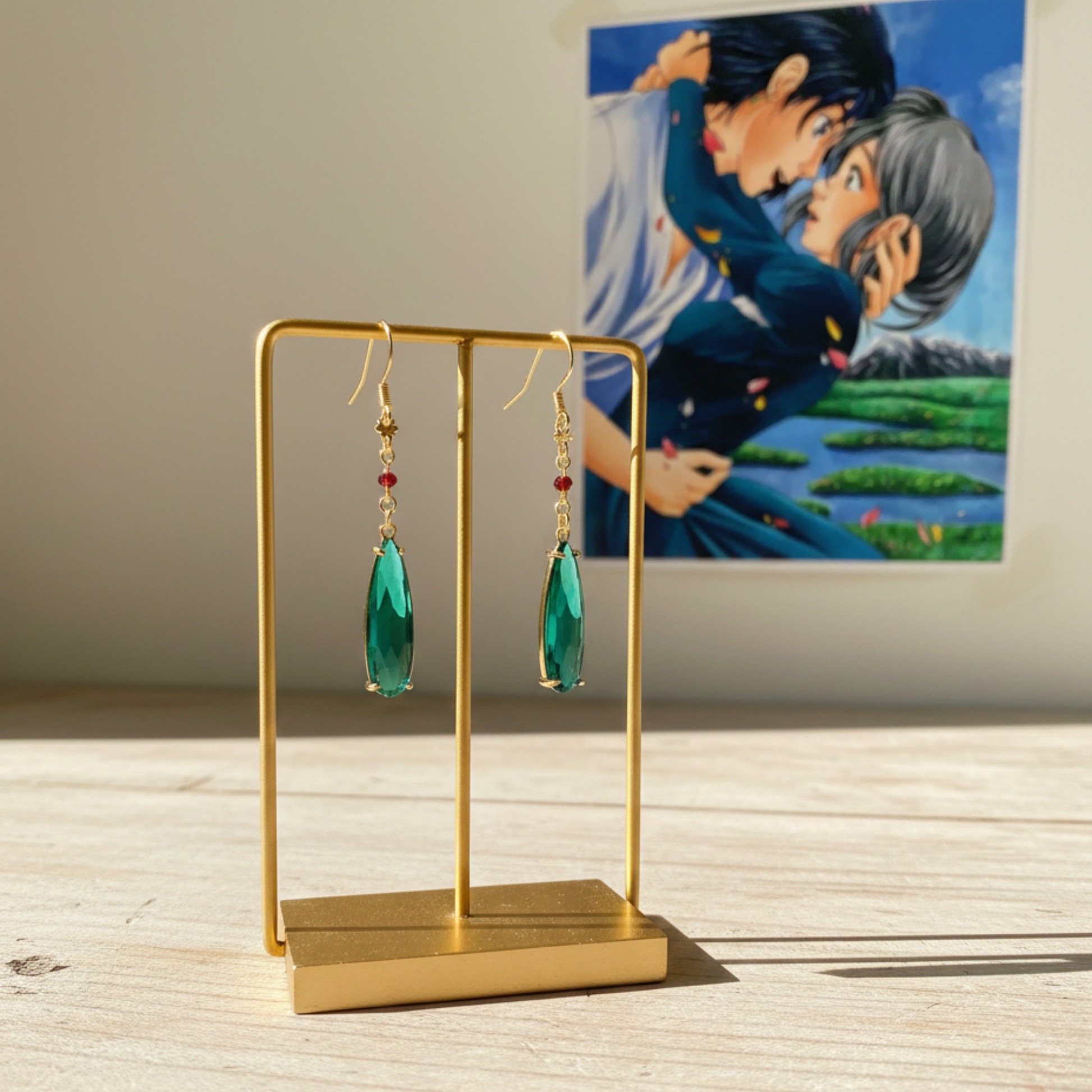 Coppia di orecchini a monachella dorati con goccia pendente verde smeraldo e piccolo cristallo rosso, ispirati al personaggio Howl de Il Castello Errante di Howl, gioielli cosplay eleganti.